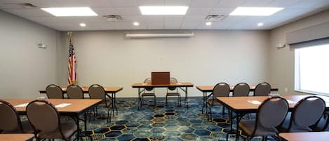 A conference room with hexagonal carpet pattern, wooden tables, and chairs, an American flag, and a projector screen.