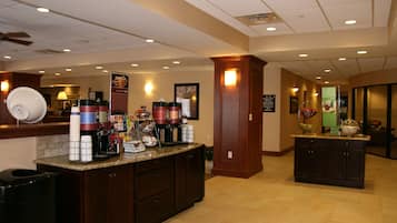 A hotel lobby with a reception desk, a coffee station, and a large mirror.
