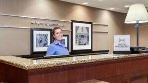 Un comptoir d’accueil avec une pancarte « Bienvenue à Watertown », des photos encadrées et une pancarte « Hilton Honors ».