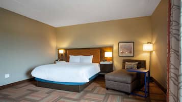 A hotel room with a large bed, a small armchair, a bedside table with a lamp, and a wall-mounted picture.