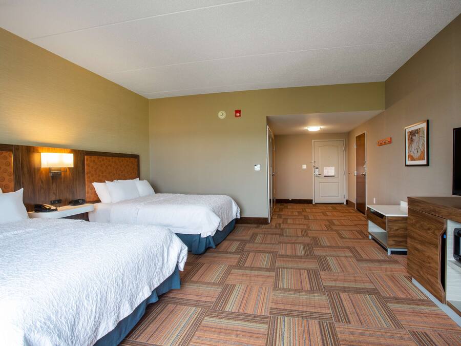 A hotel room with two beds, a desk, a television, and a microwave.
