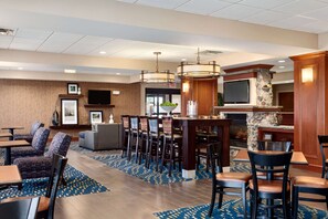 Un hall d’hôtel comprenant un bar, des espaces aménagés avec des sièges et un téléviseur fixé au mur.