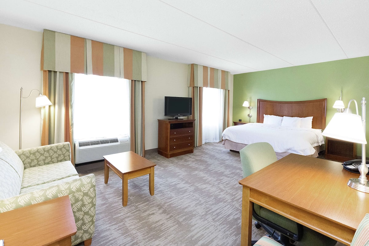 Una habitación de hotel con cama, escritorio, silla, televisión y lámpara.