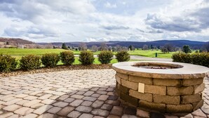 A stone fire pit in a paved outdoor area with a view of a green landscape and distant hills. - Hampton Inn & Suites Blairsville (Blairsville)