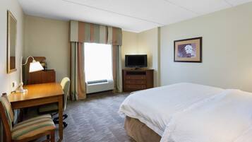A hotel room with a bed, a desk with a chair, a television, and a framed picture on the wall.