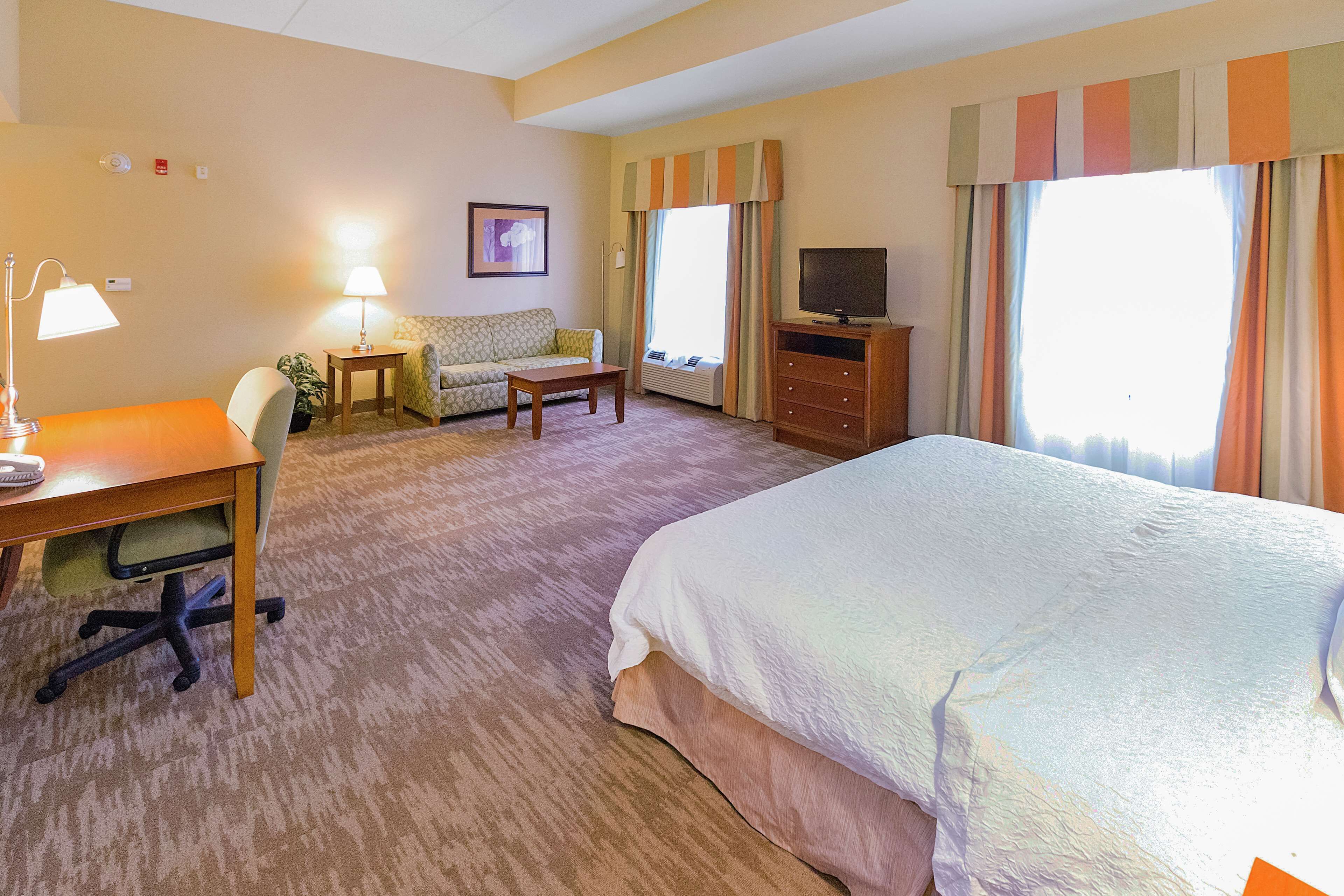 A hotel room with a bed, a desk with a lamp, a sofa, a television, and a window with curtains.