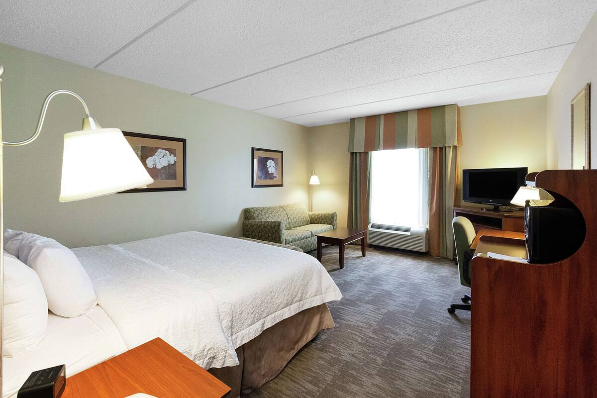 Una habitación de hotel con una cama, un escritorio con ordenador, una silla, una lámpara y un televisor.