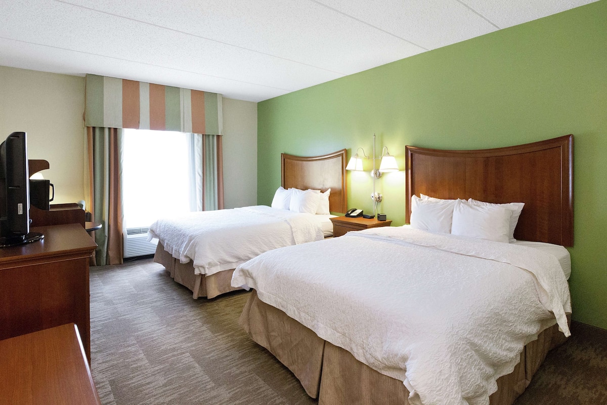 Habitación de hotel con dos camas, un escritorio, un televisor y una ventana con cortinas.