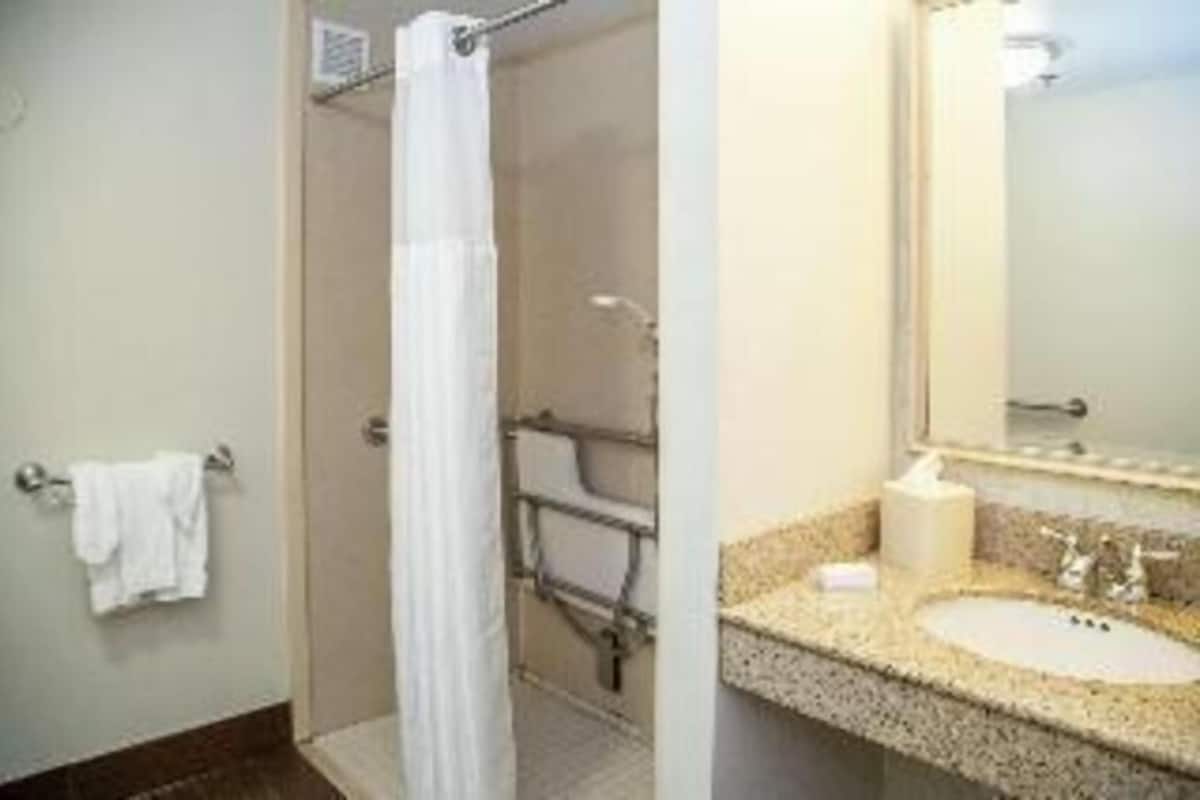 Un baño con ducha, lavabo, espejo y toallero.