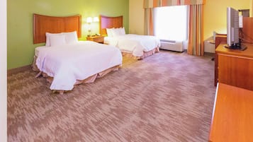A hotel room with two beds, a desk, a television, and an air conditioning unit.