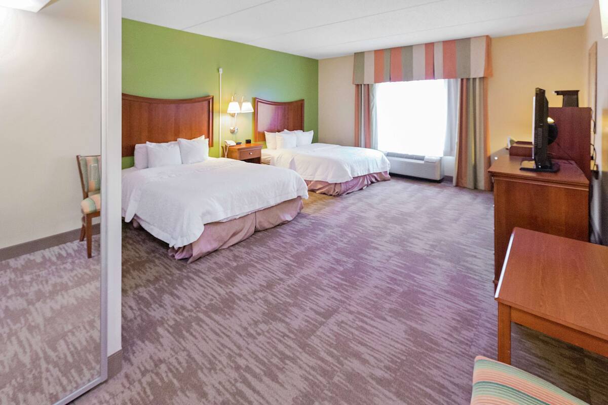 Habitación de hotel con dos camas, un escritorio, una silla, un televisor y una ventana con cortinas.