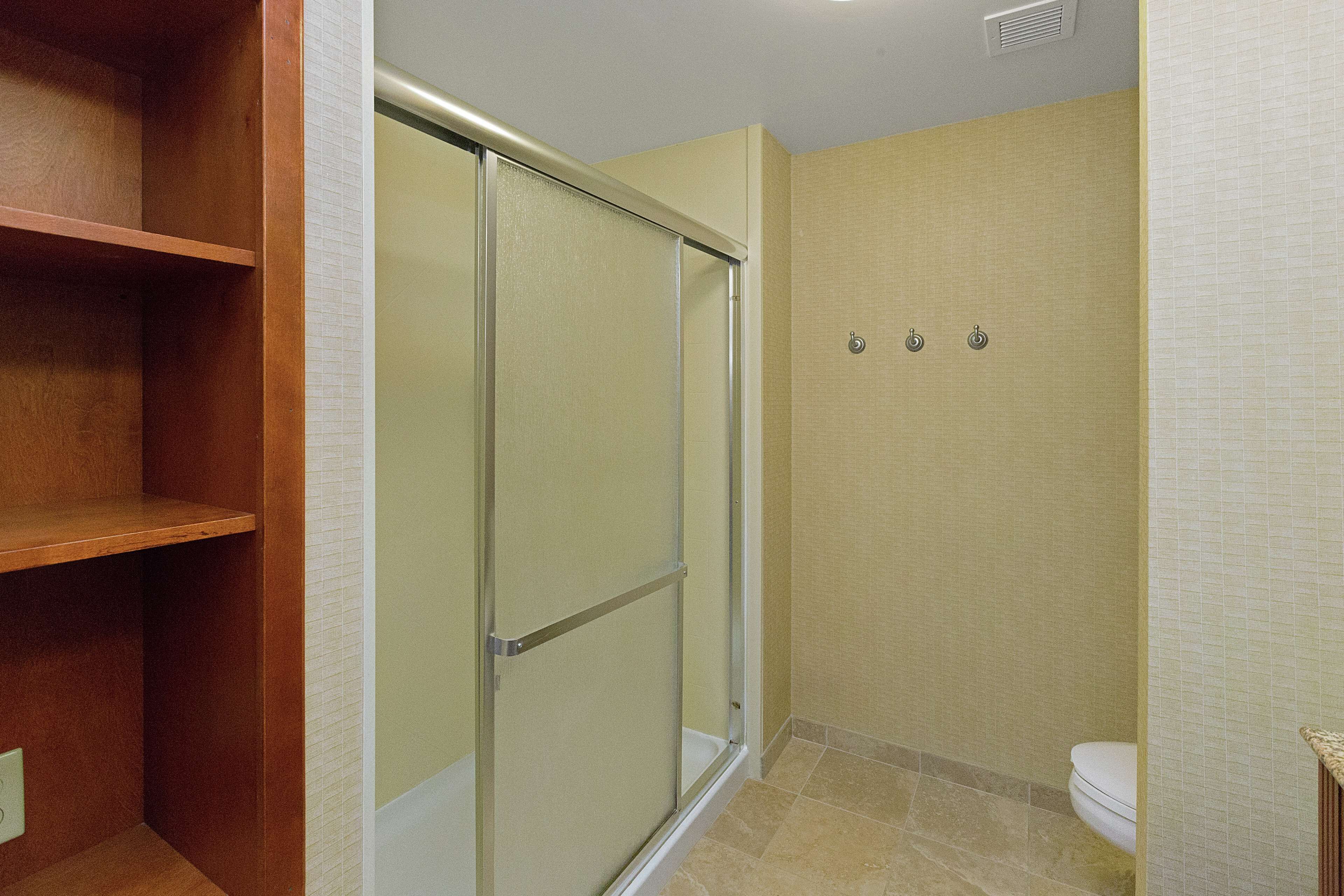 Un bagno con box doccia in vetro, un water e uno scaffale in legno.