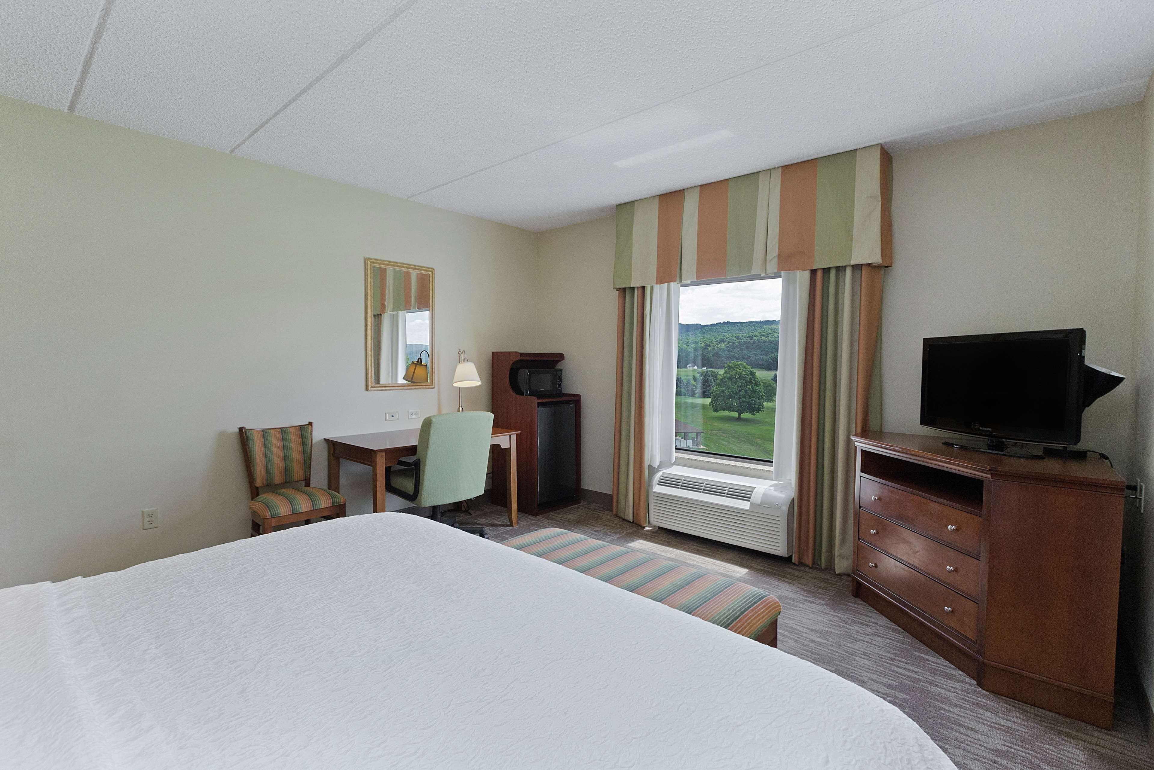 Ein Hotelzimmer mit Bett, Schreibtisch mit Stuhl, Fernseher und einem Fenster mit Vorhängen.