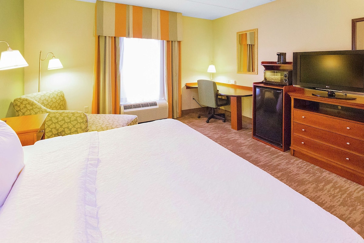 Habitación de hotel con una cama grande, un escritorio con silla, televisión, microondas y lámpara.