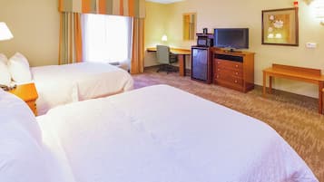 Habitación de hotel con dos camas, un escritorio con computadora, televisión y un mueble bajo.