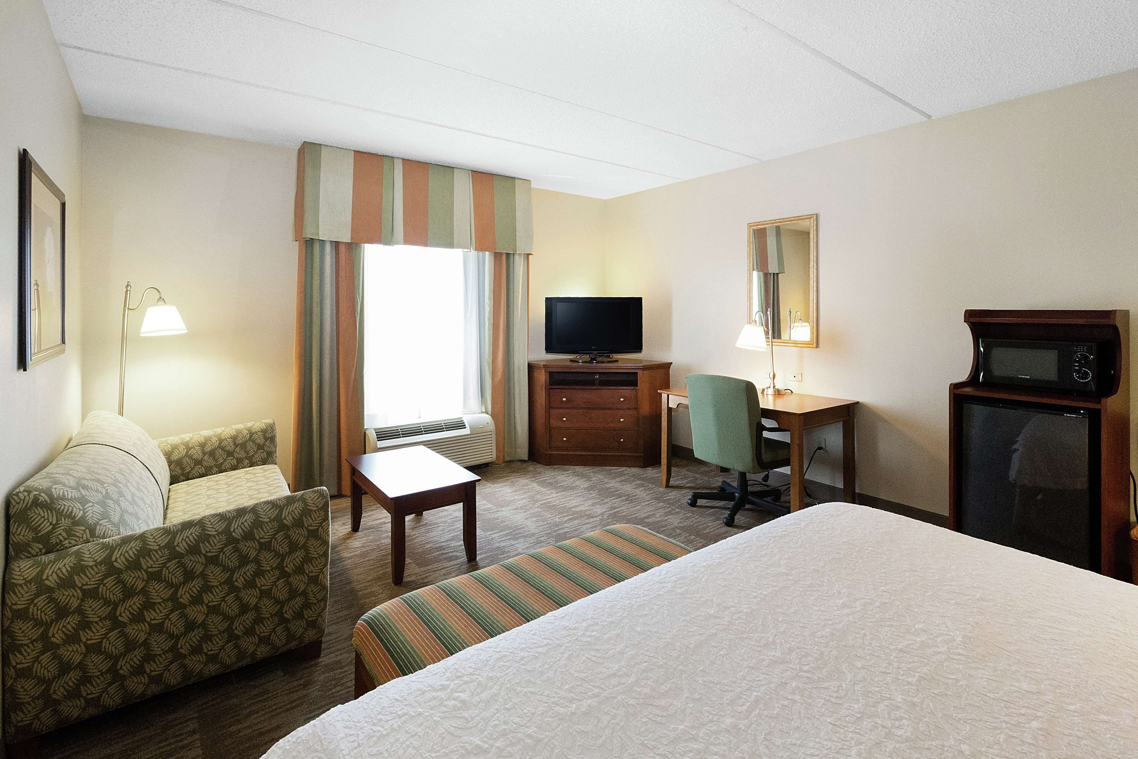 Ein Hotelzimmer mit einem Bett, einer Couch, einem Schreibtisch mit Stuhl, einem Fernseher, einer Mikrowelle und einem Fenster mit Vorhängen.