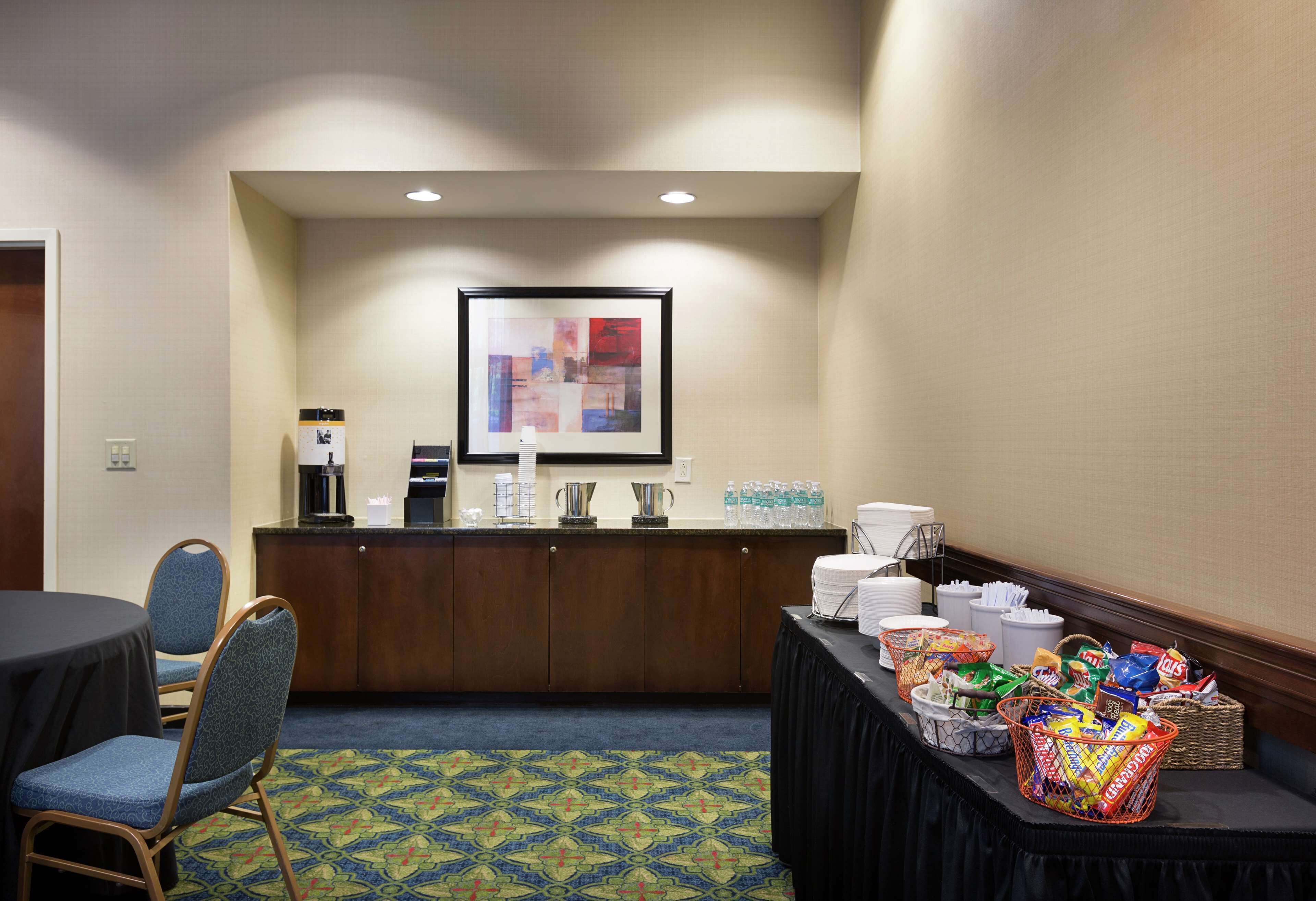 Ein Hotel-Rezeptionsbereich mit Empfangsschalter, Sitzgelegenheiten, einer Kaffeestation und einem Bufett mit Snacks.