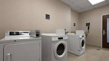 Un área de lavandería con dos lavadoras y secadoras de carga frontal, un dispensador de toallas de papel y un teléfono en la pared.