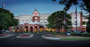 A Hampton Inn hotel with a brick facade, multiple arches, and a flagpole. - Hampton Inn Charlotte-Belmont at Montcross (Belmont)