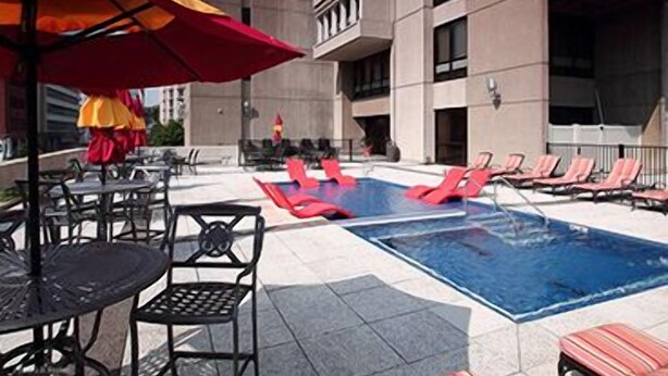 A rooftop pool area with lounge chairs and tables, surrounded by a high-rise building. - Pointe 400 by ExecuStay (St. Louis)