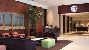 A modern lobby with a dark-colored sofa, a green ottoman, and a large plant. A reception desk is visible in the background. - Pointe 400 by ExecuStay (St. Louis)