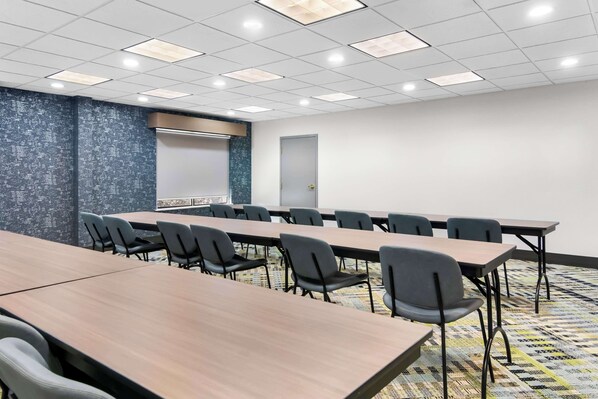 A conference room with a long table, chairs, a projector screen, and a door. - Big Country Hotel & Suites, SureStay Collection by BW (Abilene)