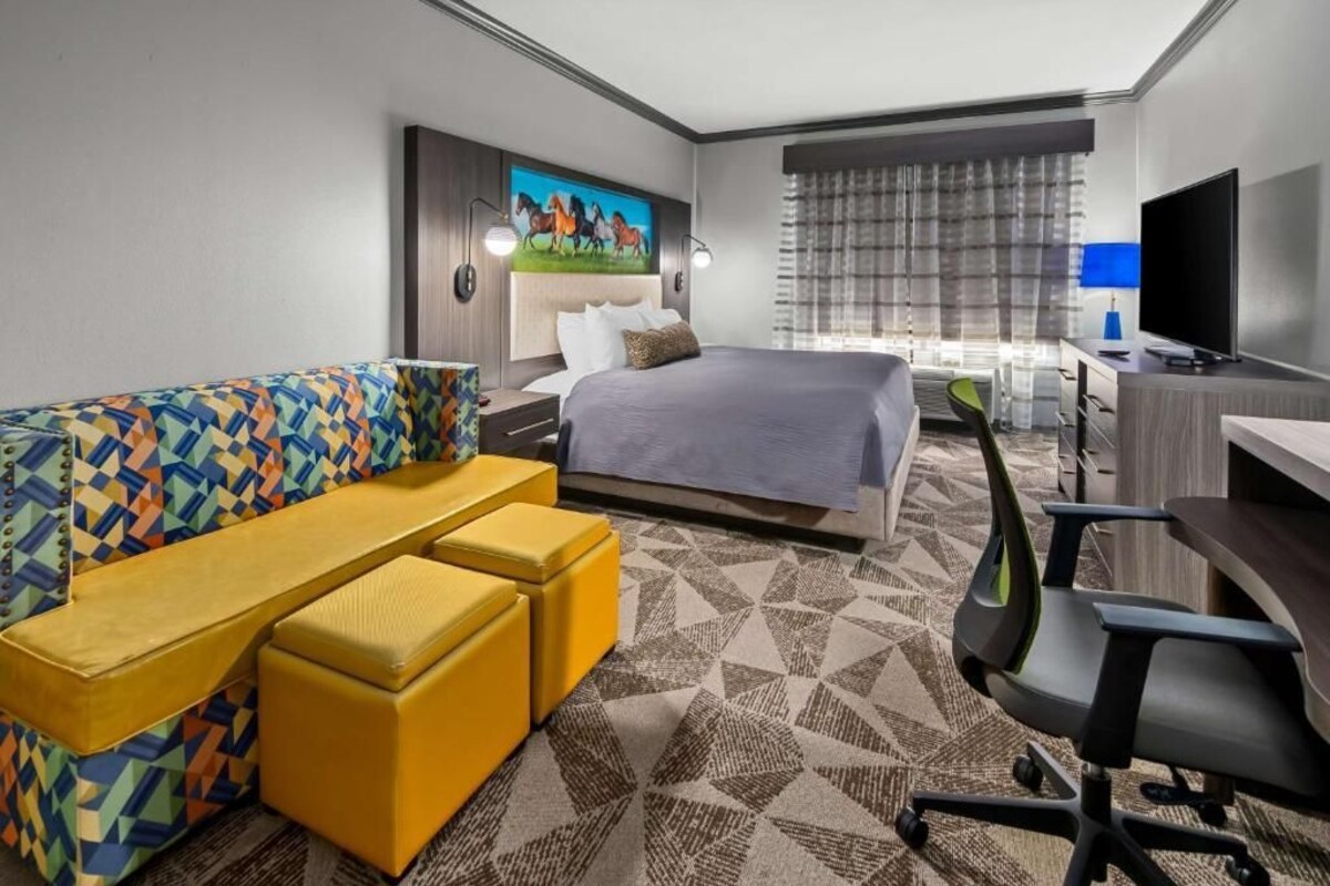 A hotel room with a bed, a sofa, a desk, a TV, and a painting on the wall.