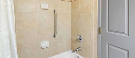 A bathroom with a bathtub, a handrail, and a door.
