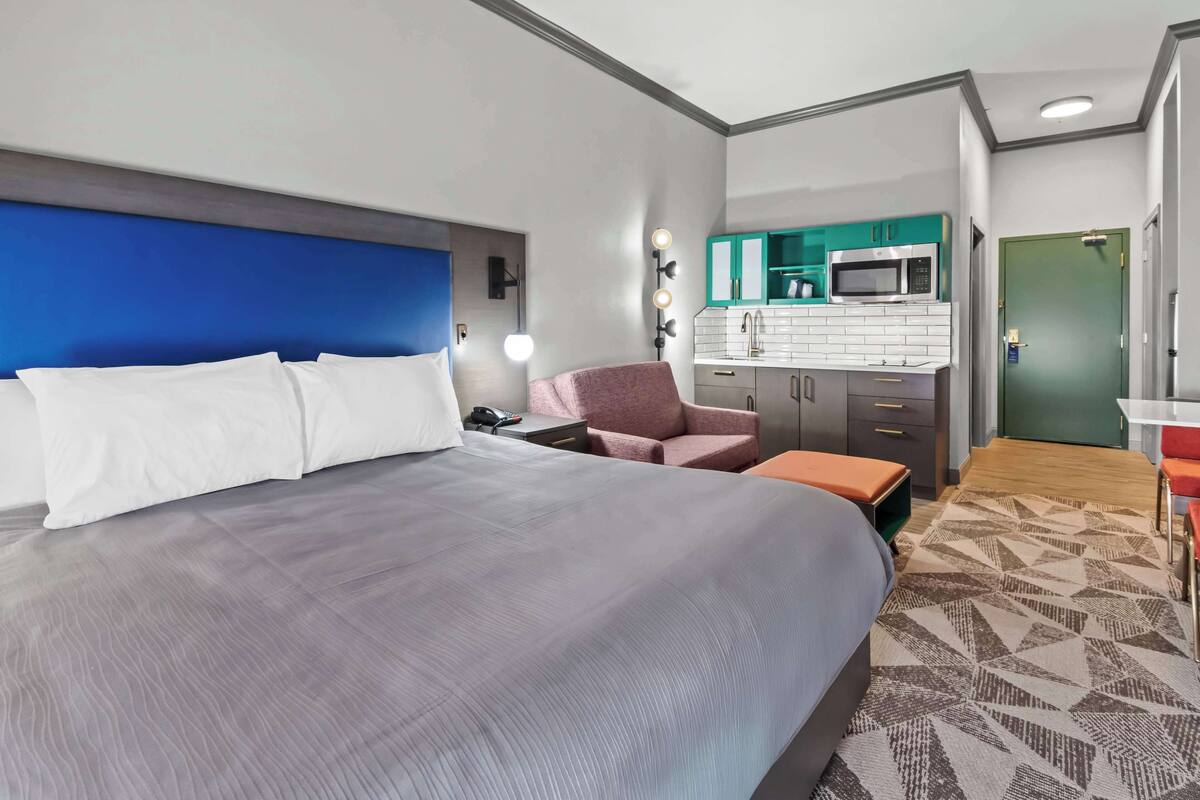Quarto de hotel com uma cama grande, uma escrivaninha, uma cadeira, micro-ondas e cozinha compacta.