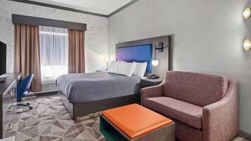 Quarto de hotel com uma cama, escrivaninha, cadeira e sofá.