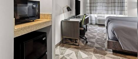 Een hotelkamer met kitchenette, een bed, een bureau met computer en een groot raam met gordijnen.