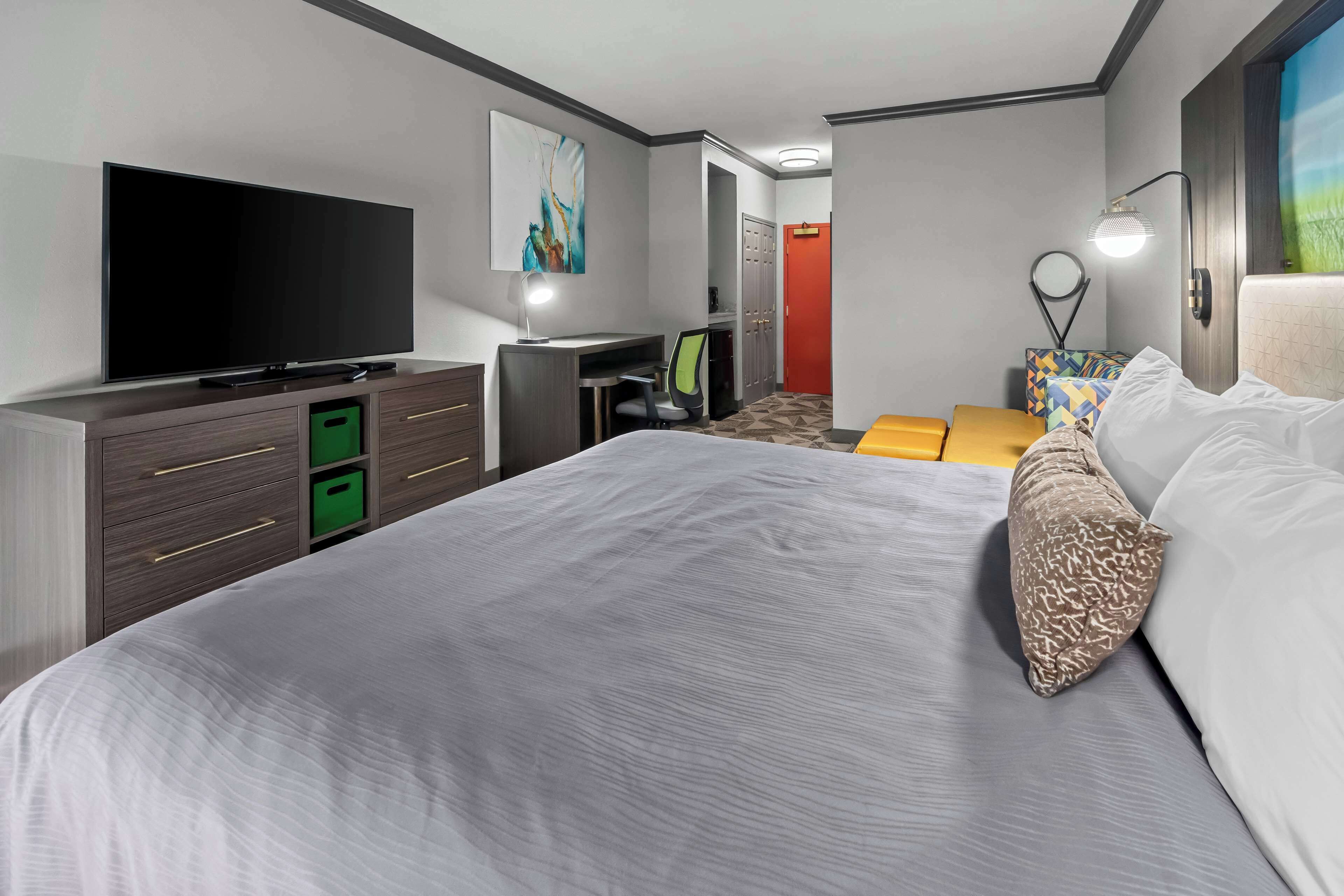 A modern hotel room with a large bed, a flat-screen TV, a desk with a chair, and a wardrobe.