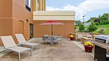 Un patio al aire libre con sillones de descanso, una mesa, una sombrilla y una parrilla.