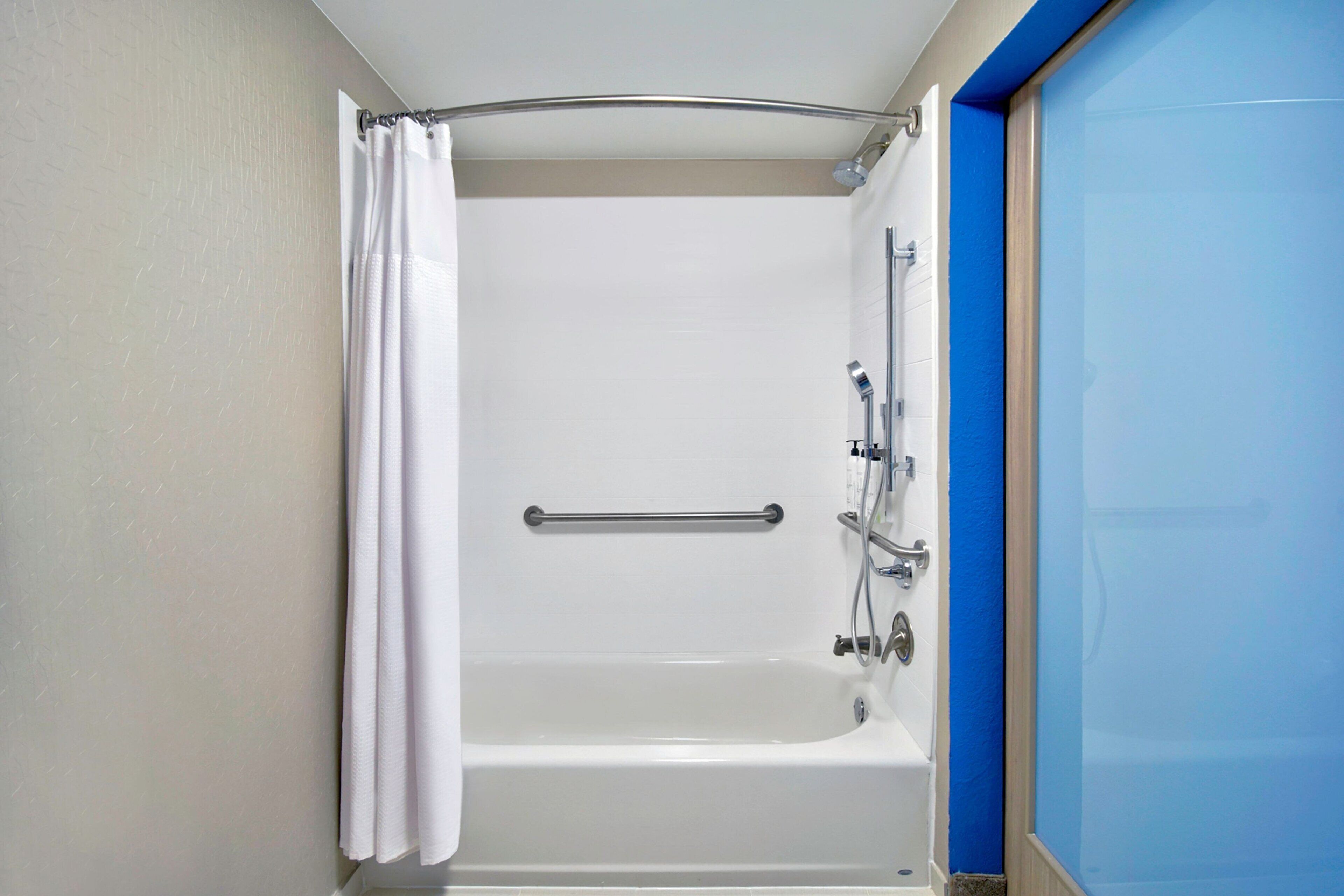 A bathroom with a bathtub, a shower curtain, and a grab bar.