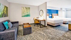Habitación de hotel con sofá gris, escritorio, cama y un espejo grande.