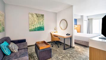 A hotel room with a sofa, a desk, a bed, and artwork on the walls.