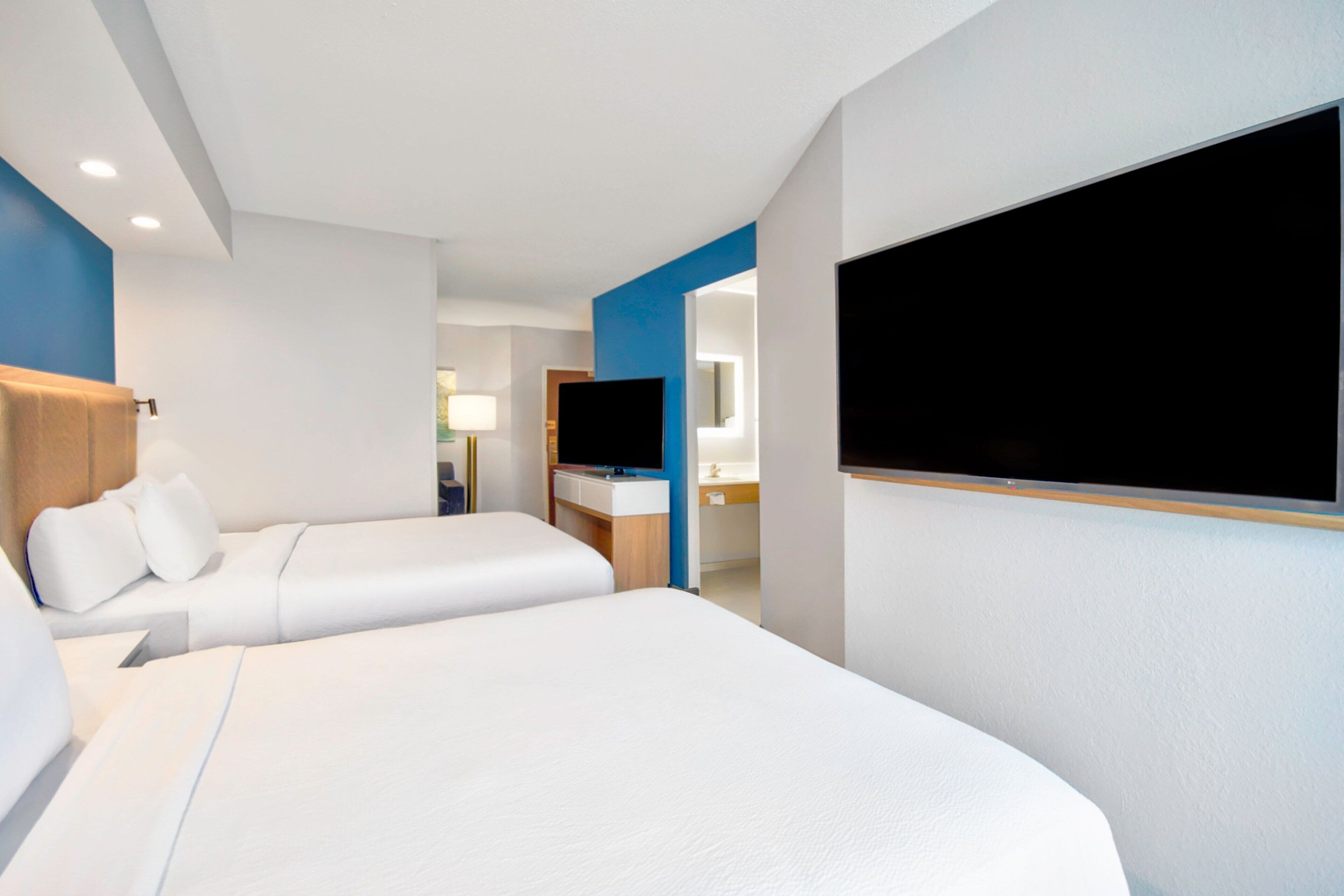A hotel room with two beds, a TV, a desk, and a bathroom visible through an open door.