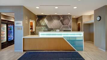 A hotel reception area with a modern design, including a reception desk, a clock, and a refrigerator stocked with beverages.