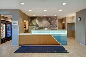 A hotel reception area with a modern design, including a reception desk, a clock, and a refrigerator stocked with beverages. - Springhill Suites by Marriott Erie (Erie)