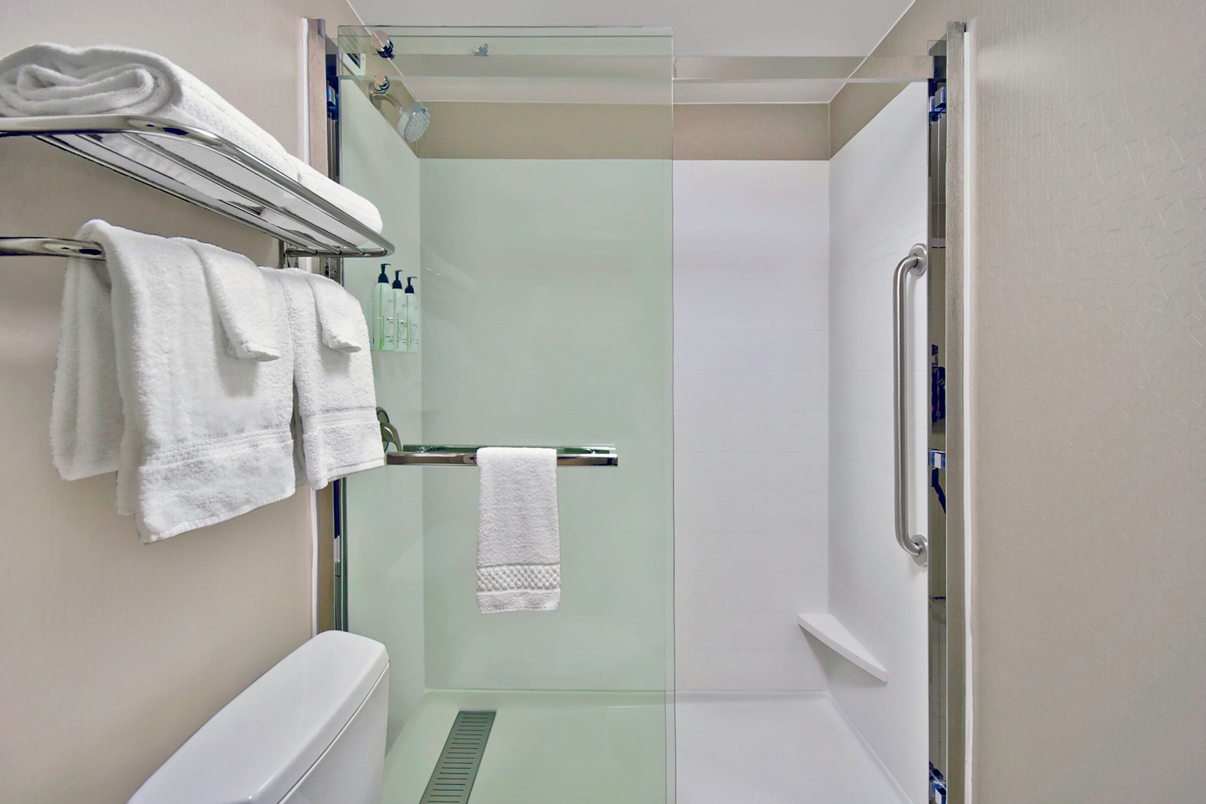 Une salle de bain moderne avec une douche à parois de verre, un porte-serviettes avec des serviettes pliées et une bouteille de shampoing bien en évidence.