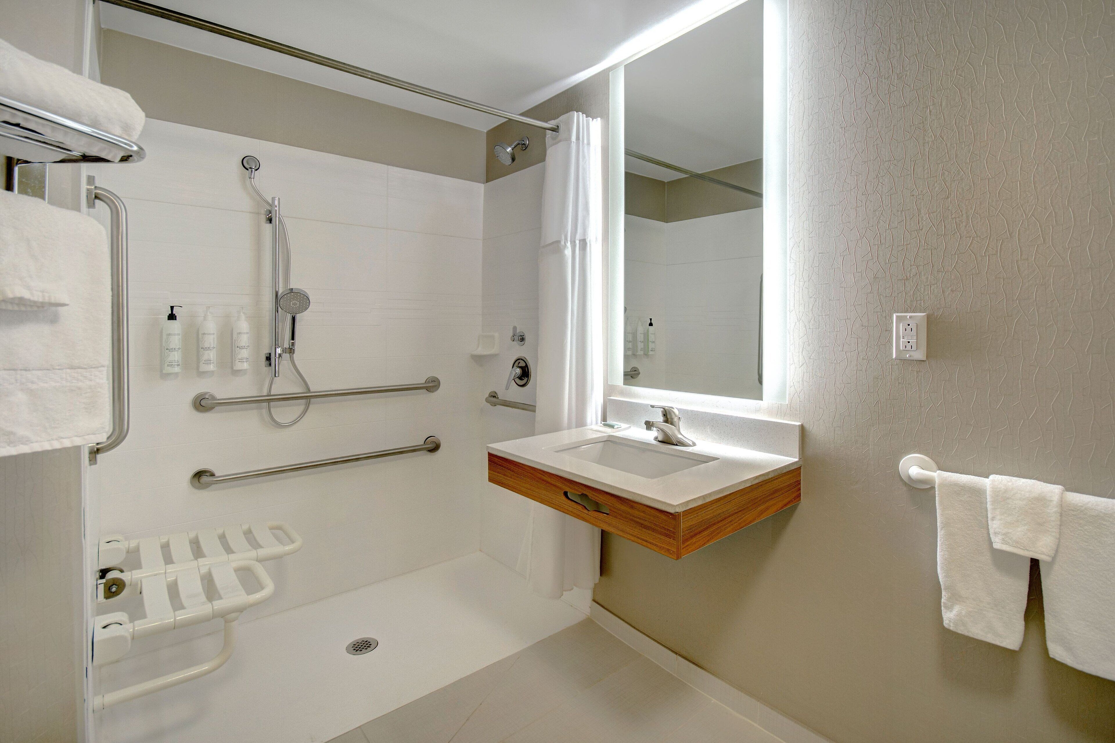 A modern bathroom with a shower, grab bars, a sink, and a towel rack.