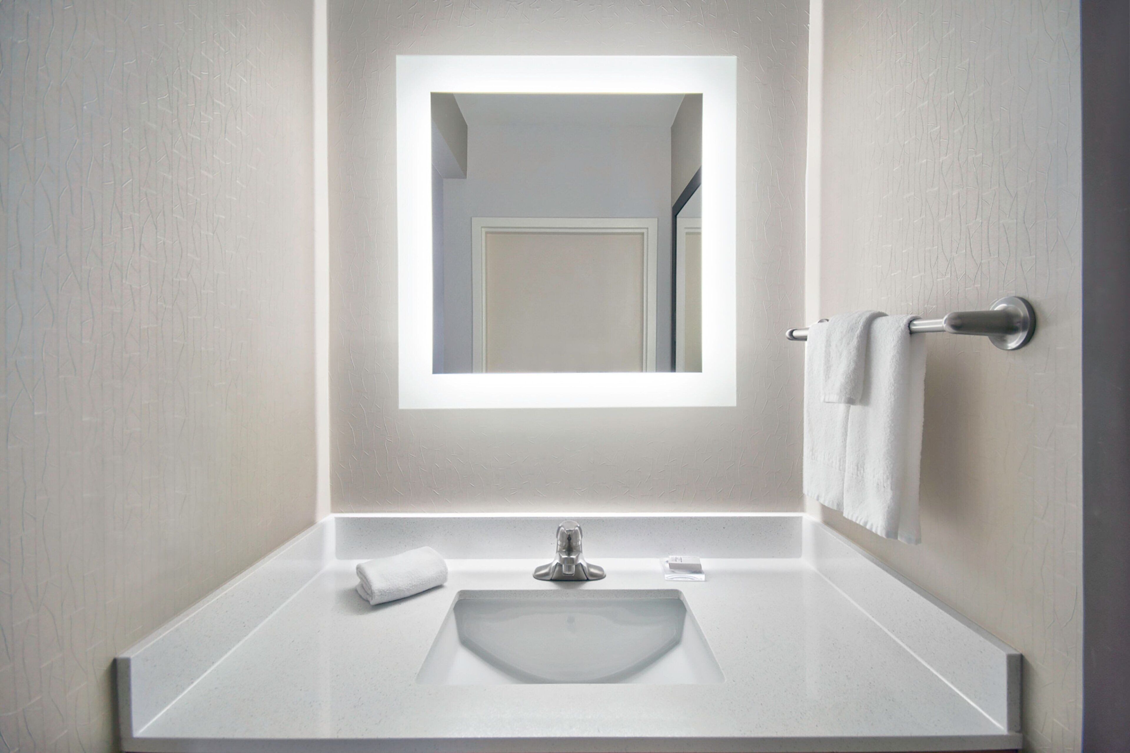 A modern bathroom with a rectangular mirror, a white sink, and a towel rack.