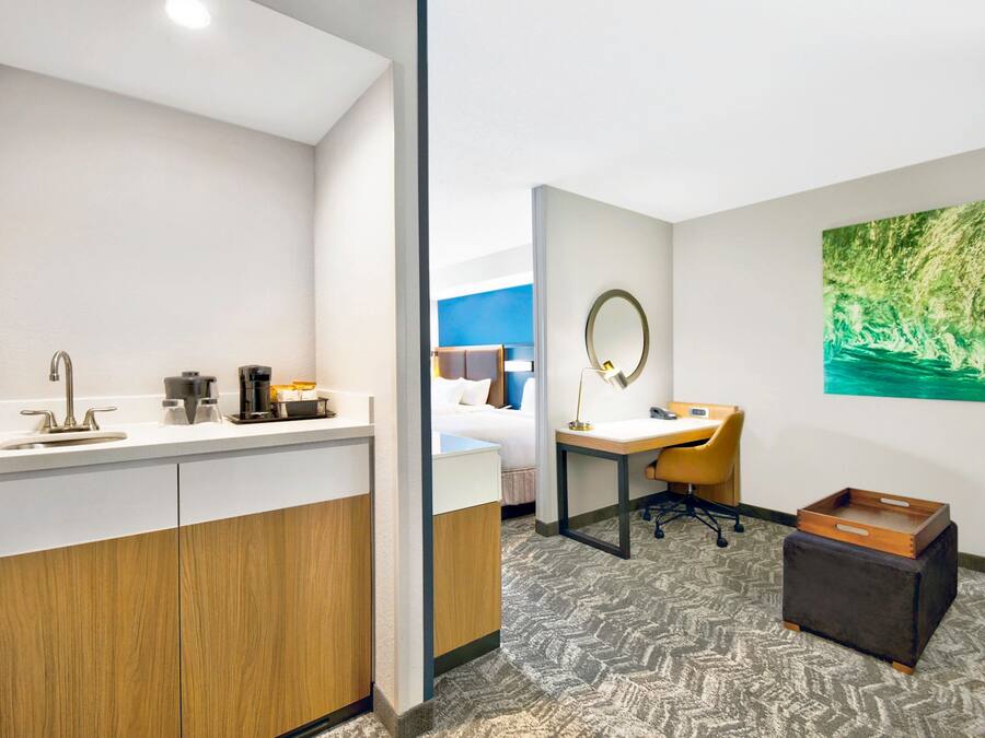 A modern hotel room with a bathroom, a desk, and a bed.