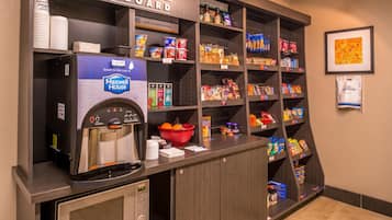 A kitchenette area with a coffee machine, a bowl of fruit, and various snacks and condiments.