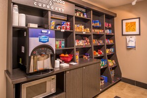 Una kitchenette con una cafetera, un tazón de fruta y diferentes bocadillos y condimentos.