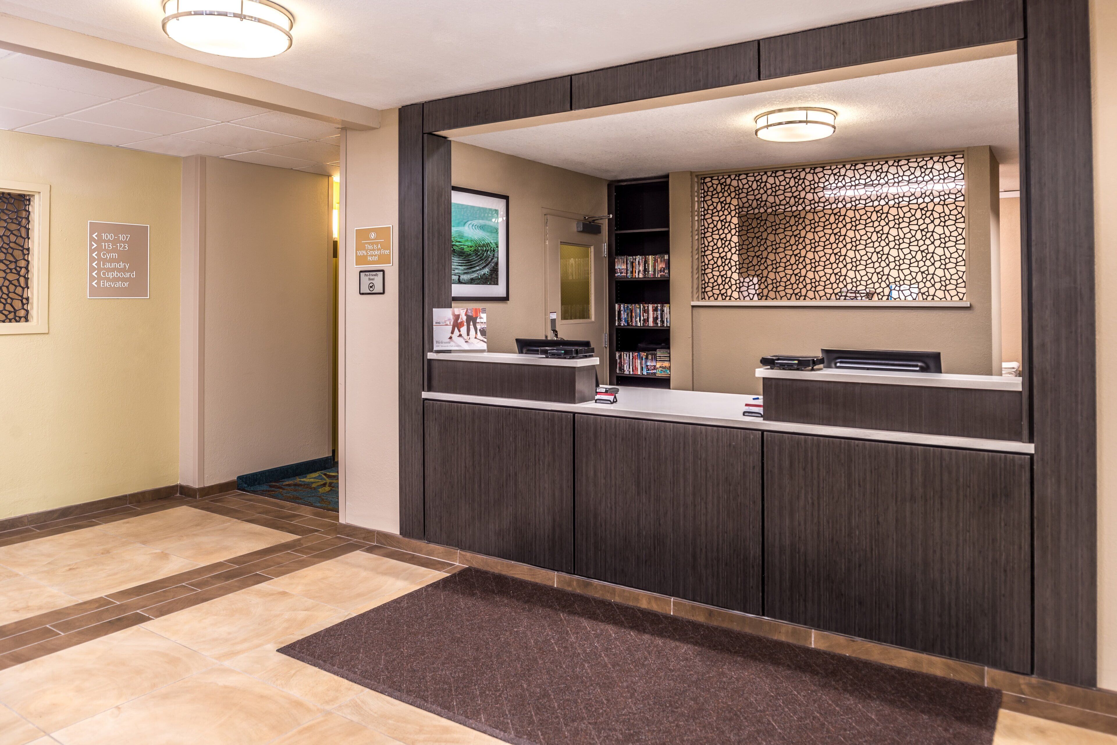 Een hotel receptie met een receptiebalie, een aan de muur bevestigde televisie en een decoratief muurpaneel.