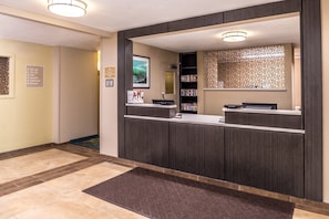 Zona de recepción de hotel con mostrador, televisor montado en la pared y un panel decorativo.