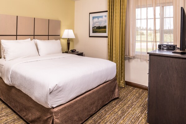 A hotel room with a bed, a nightstand, a lamp, a television, and a window with curtains.