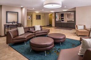 Un moderno vestíbulo de hotel con un sofá modular, otomanos redondos, un mostrador de recepción y una zona de bar.