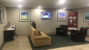 A reception area with a beige sofa, black chairs, a desk with a computer, and framed pictures on the walls. - Candlewood Suites Kansas City Speedway by IHG (Kansas City)